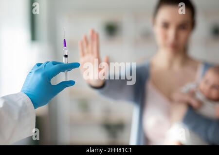 Esitazione del vaccino. Donna con neonato che rifiuta la siringa in mano del medico Foto Stock