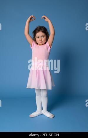 Una graziosa ballerina che esegue pose in balletto, in piedi isolati su sfondo blu con spazio di copia Foto Stock