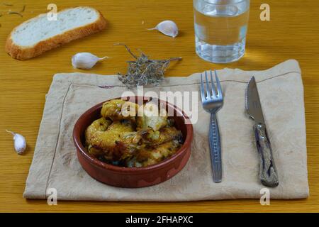 Ali di pollo all'aglio (Pollo al ajillo). Piatto di Tapa spagnola in una ciotola di argilla servita con pane croccante, ricci d'argento e un bicchiere d'acqua Foto Stock