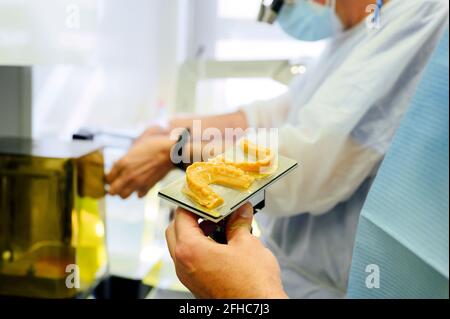 Vista laterale del dentista maschio non riconoscibile del raccolto in uniforme vicino collega con calchi a mascelle e fresatrice medica in ospedale Foto Stock