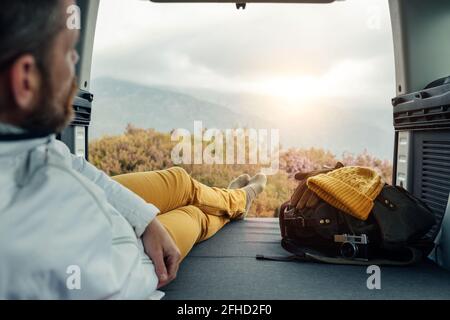 Vista posteriore di un camper maschio irriconoscibile in outerwear seduto sopra furgone e vista panoramica delle highlands Foto Stock