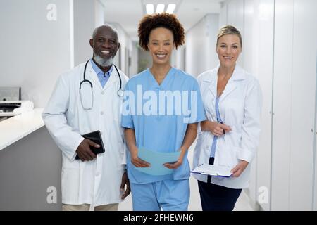 Ritratto di tre diversi medici maschili e femminili in piedi corridoio ospedaliero sorridente alla telecamera Foto Stock