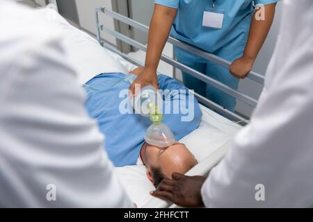 Diversi medici maschili e femminili che mettono maschera di ossigeno sul paziente sdraiato a letto Foto Stock