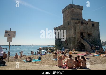 Il Castello di Rapallo è iconico per la sua posizione eccezionale sulle rocce. Vicino, la gente del posto e i turisti godono il sole su una piccola spiaggia di sabbia. Foto Stock