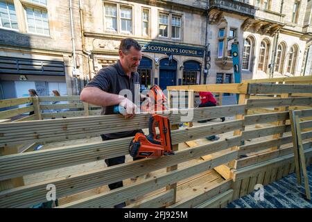 Edimburgo, Scozia, Regno Unito. 25 aprile 2021. Scene dalle strade del centro di Edimburgo la domenica pomeriggio del giorno prima che negozi e aziende non essenziali possano riaprirsi in Scozia sotto il rilassato regole di blocco del covid-19. Fig. I falegnami che hanno rifinito una piattaforma esterna ridisegnata per i posti a sedere presso lo Scotsman's Lounge di Cockburn Street.la piattaforma originale a un livello non soddisfaceva le regole di controllo degli edifici e ora è stato costruito un design a gradini. Iain Masterton/Alamy Live News Foto Stock