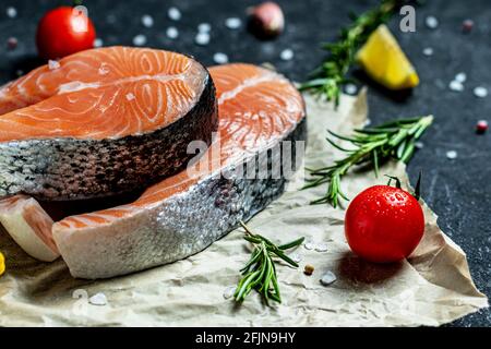 Due bistecche di salmone fresco crudo con sale, peperoni, limone, pomodori e rosmarino sulla carta rustica Foto Stock