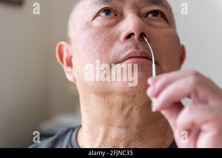 Un uomo asiatico maturato che preleva un campione di tampone eseguendo un test di auto-abitazione Covid-19. Foto Stock