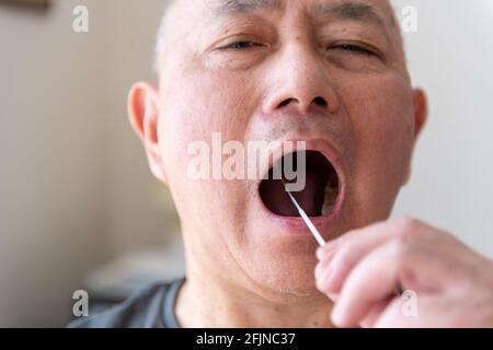 Un uomo asiatico maturato che preleva un campione di tampone eseguendo un test di auto-abitazione Covid-19. Foto Stock