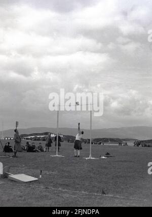 1956, un concorrente maschile di un highland games, Grenock, Scozia, Regno Unito, gettando un peso su una barra alta, noto come l'evento 'peso sopra la barra'. Documentati per la prima volta negli anni 1820 a Invergarry, i giochi vedevano i locali dimostrare la loro forza e agilità in varie attività, come il lancio di un caber, il lancio di un martello, oltre alla danza scozzese e le piping. La visita della Regina Vittoria al raduno di Braemer nel 1848 ha iniziato la Royal Association e li ha visti aumentare la popolarità. Nei mesi estivi, in tutta la Scozia si tengono vari eventi noti come Highland Games o semplicemente riunioni. Foto Stock