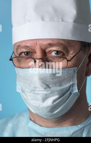 Ritratto di un medico esperto di mezza età in un cappuccio medico e maschera, indossando occhiali. Vista ravvicinata della fotocamera Foto Stock