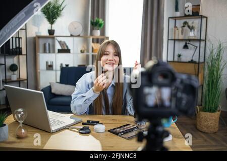 Bella giovane donna che prende circa i trattamenti di cura della pelle mentre si siede a tavola con i vari cosmetici. Beauty blogger registrazione online tutorial su videocamera. Foto Stock