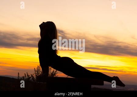 Silhouette di una giovane donna che fa la posa del cobra al tramonto Foto Stock