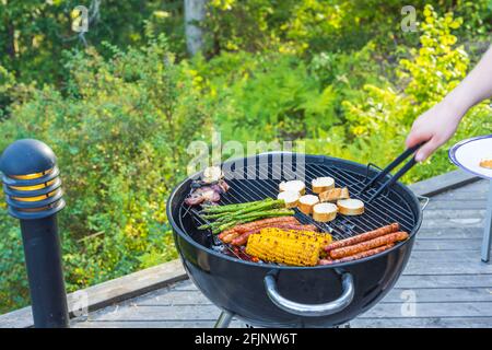 Vista ravvicinata delle mani dell'uomo che grigliano gli alimenti sulla griglia a carbone. Svezia. Foto Stock