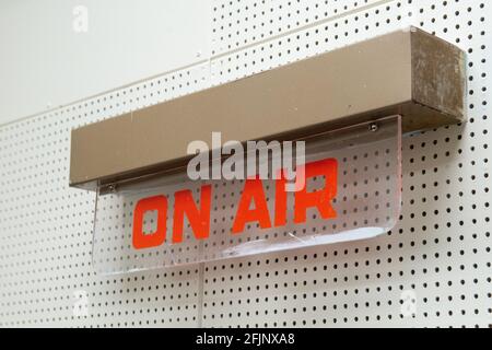 Un cartello radiomobile vintage apposto su un pannello a parete bianco. Il cartello illuminato in vetro ha una scritta rossa con le parole sull'aria. Foto Stock