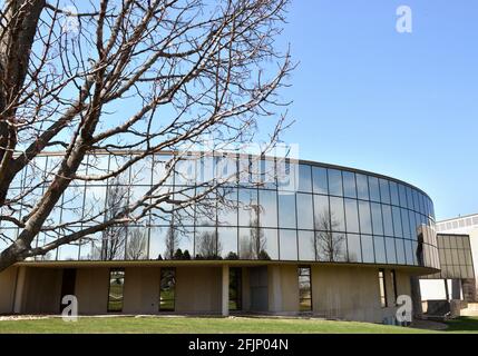 Edificio in vetro curvo nel campus dell'Hawkeye Community College che mostra i riflessi del cielo, delle nuvole e degli alberi durante la primavera. Foto Stock