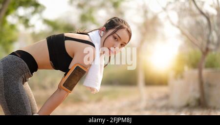 ripresa di una giovane bella atleta asiatica che riposa dopo aver fatto jogging con gli auricolari contro al parco. Foto Stock