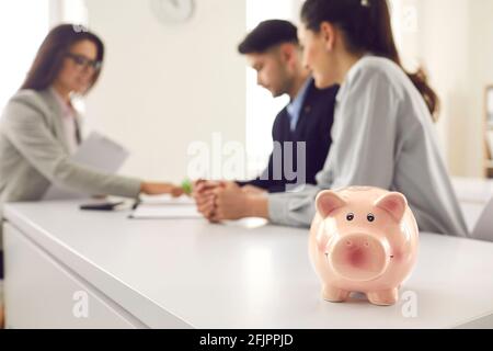 Piggy banca sul banco dei mediatori di prestito in su vicino, coppia firma il contratto in background Foto Stock