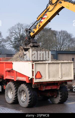 Un grande escavatore giallo con gru raccoglie la sabbia dalla parte posteriore di un autocarro in un cantiere. Immagine verticale Foto Stock