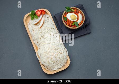 Ideyappam o noolappam, prodotto per la colazione dell'India del sud fatto usando riso crudo che è disposto in una base di servire di legno con uovo masala come buona combinazione Foto Stock