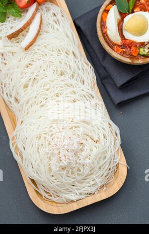 Ideyappam o noolappam, prodotto per la colazione dell'India del sud fatto usando riso crudo che è disposto in una base di servire di legno con uovo masala come buona combinazione Foto Stock