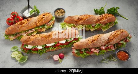 Dall'alto di appetitosi panini baguette appena fatti ripieni prosciutto e formaggio con verdure fresche ed erbe in grigio tabella Foto Stock