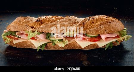 Gustoso sandwich di prosciutto e formaggio con verdure in mezzo metà del pane fresco su un tavolo di legno nero Foto Stock