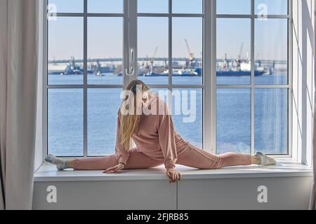 Allenamento domestico di ragazza cheerleader, giovane donna flessibile fare esercizio stretching per fare splits. Foto Stock