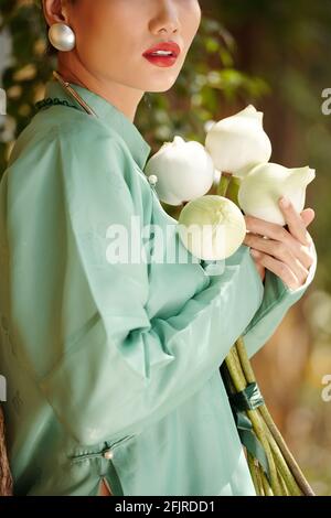 Immagine ritagliata di bella giovane donna in piedi all'aperto con chiuso fiori di loto in piedi nel parco Foto Stock