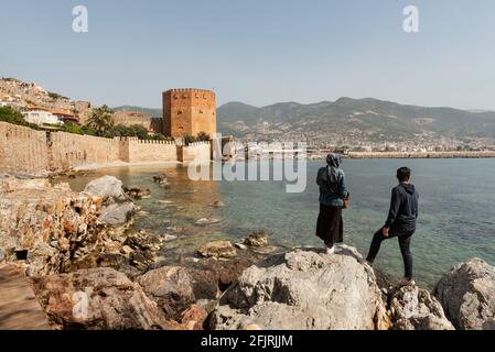 Alanya, Turchia. 7 Aprile 2021 i turisti turchi godono della vista delle antiche mura del castello di Alanya e della Torre Rossa sulla costa mediterranea di T. Foto Stock