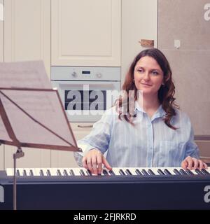 Donna che guarda lo stand musicale con note musicali e il gioco sintetizzatore domestico Foto Stock