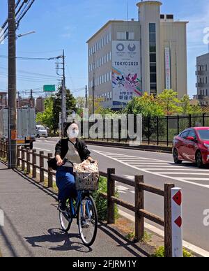 Tokyo, Giappone. 22 Apr 2021. NESSUNA VENDITA IN GIAPPONE! Le mascotte olimpiche Miraitowa e Someity sono mostrate su un banner presso il municipio di Niiza City, qui si svolgono le gare olimpiche di tiro, feature, foto simbolica, motivo di confine, in primo piano un ciclista con una maschera, Le Olimpiadi estive 2020 a Tokyo/Giappone si terranno a Tokyo dal 23 luglio all'8 agosto 2021, NESSUNA VENDITA IN GIAPPONE! | utilizzo in tutto il mondo credito: dpa/Alamy Live News Foto Stock