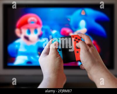 Il giocatore maschile si accingia al controllo della console che gioca a un videogioco o a un videogioco su un grande schermo o su una TV. Punto di vista o pov del controller di gioco nelle mani davanti o Foto Stock