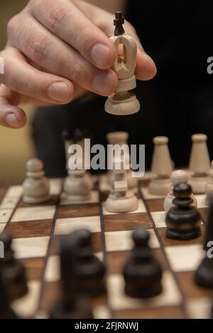 Uomo che prende il passo successivo sul gioco degli scacchi. Mano umana che muove il re degli scacchi bianchi di legno Foto Stock