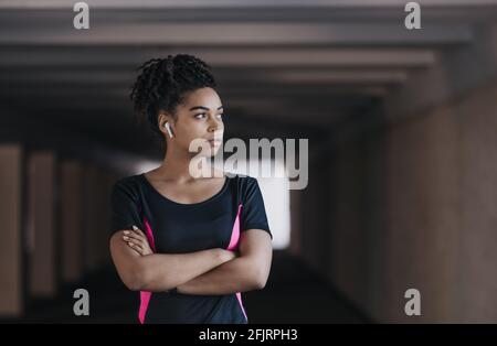 Ritratto di giovane, atletica e attraente donna afroamericana in abbigliamento sportivo e cuffie wireless Foto Stock