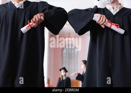 Una visione tronca dei laureati multietnici con diplomi che fanno un balzo Foto Stock