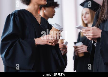 Laureati multietnici che tengono il caffè in viaggio e smartphone Foto Stock