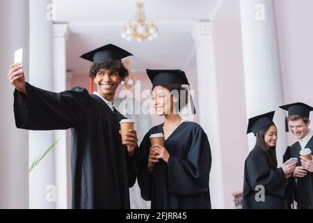 Sorridente diplomati afroamericani che prendono selfie e tengono tazze di carta Foto Stock