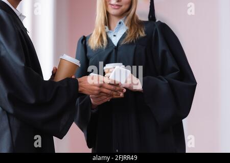 Vista ritagliata del laureato afroamericano che tiene il cellulare vicino ad un amico con caffè sempre in movimento Foto Stock