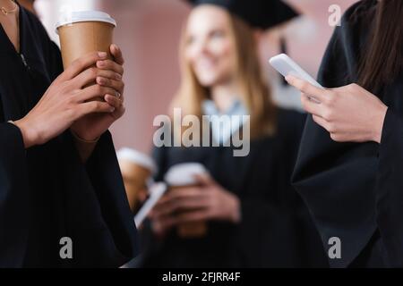 African american Bachelor tenendo il caffè per andare vicino amico con smartphone Foto Stock