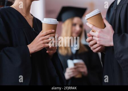 Vista ritagliata di tazze di carta nelle mani di laureati interrazziali all'università Foto Stock