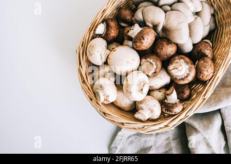 Funghi freschi champignons e funghi ostriche in cesto con tela di lino su tavola bianca, vista dall'alto. Foto Stock