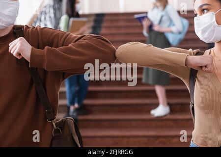 Studenti interrazziali in maschere mediche facendo pugno in università sala Foto Stock