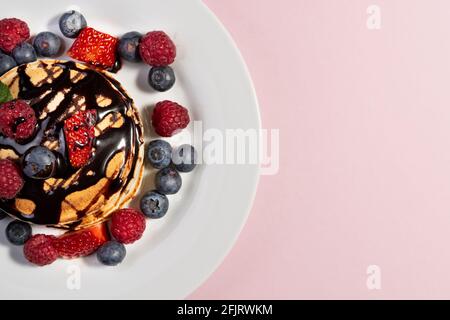 vista dall'alto di un dessert di frittelle con frutta e cioccolato su un piatto bianco su sfondo rosa. spazio copia Foto Stock