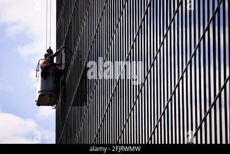 Amburgo, Germania. 26 Apr 2021. Due addetti alla pulizia in un ascensore puliscono le finestre della facciata dell'edificio Vattenfall in City Nord. Completato nel 1969, il complesso edilizio nel quartiere degli uffici City Nord di Amburgo è stato progettato dall'architetto e designer danese Arne Jacobsen. La griglia façade è composta da circa 6,500 riquadri. Credit: Christian Charisius/dpa/Alamy Live News Foto Stock