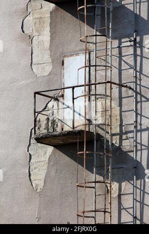 Scale di sfuggita in metallo arrugginito con tunnel di sicurezza rotondo in acciaio montato su una piattaforma di sicurezza in metallo all'esterno delle vecchie porte su lato del complesso industriale Foto Stock