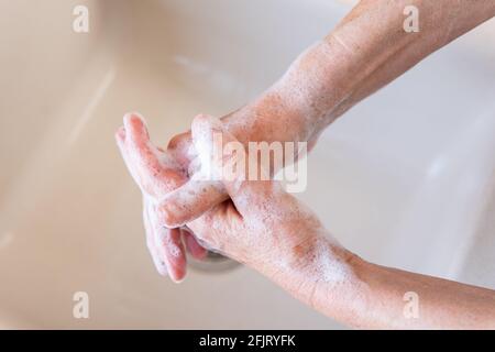 Donna anziana che le lava le mani con sapone in un lavello da cucina. Concetto di igiene personale per la prevenzione delle infezioni da virus della corona ncov (covid-19). Foto Stock