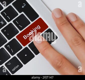 Le dita della persona che sta per premere il tasto "Booking" su una tastiera nera di un computer portatile su una scrivania dell'ufficio. Prenota/prenota alloggio, posto a sedere, volo, crociera. Foto Stock