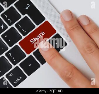 Le dita della persona stanno per premere il tasto 'Share' su una tastiera nera del computer portatile su una scrivania dell'ufficio. Condividere informazioni e dati. Foto Stock