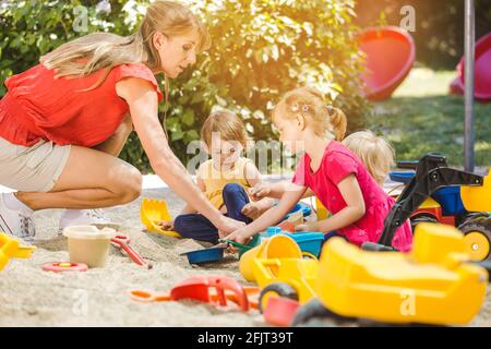 Bambini e insegnante di scuola di gioco godendo un po 'di tempo nella sabbia scatola Foto Stock