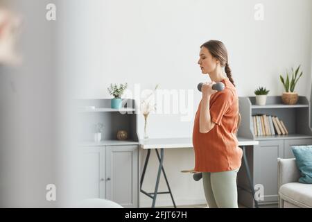 Giovane donna incinta che tiene dumbells ed esercitandosi nella mattina a casa Foto Stock